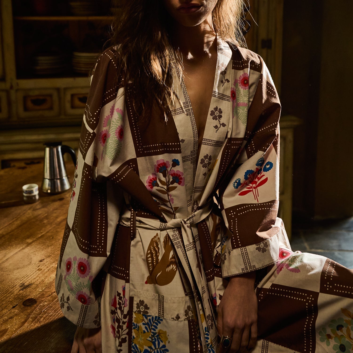 Upper body close-up of cotton robe in brown and cream checkered floral print, showing wide lapels and tied waist belt