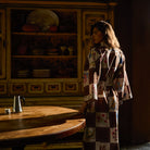 Three-quarter back view of cotton robe in brown and cream checkered floral and bird print, full length, worn loosely belted