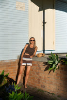 Full body view of striped knit shorts in brown, cream and blue horizontal stripes on model sitting outdoors