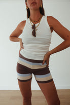Beach lifestyle shot of brown, cream and blue striped knit shorts styled with white cami top