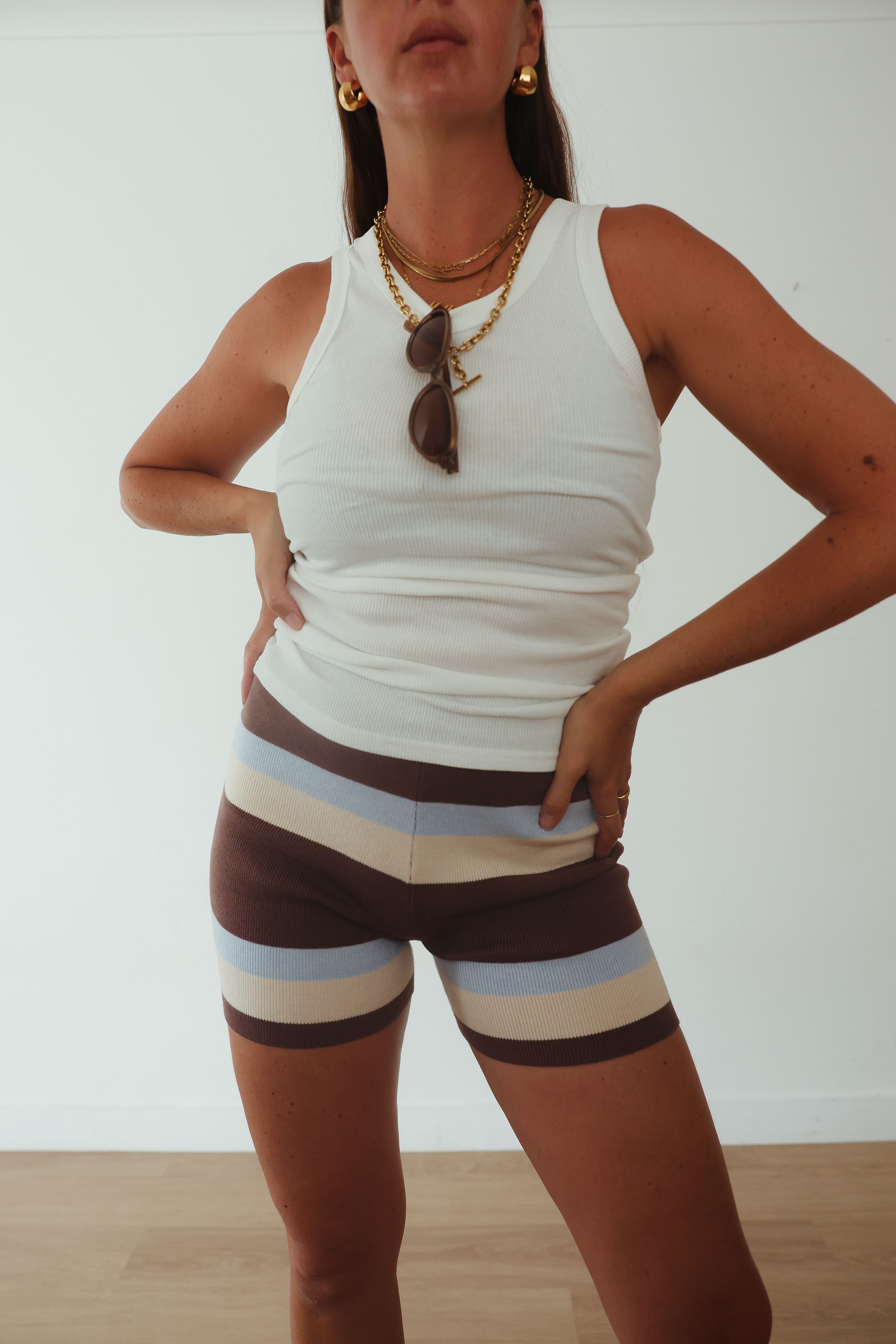 Beach lifestyle shot of brown, cream and blue striped knit shorts styled with white cami top