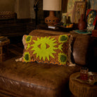 Brown patterned lumbar cushion with lime green tufted star motifs and corner sunflower details on a leather sofa