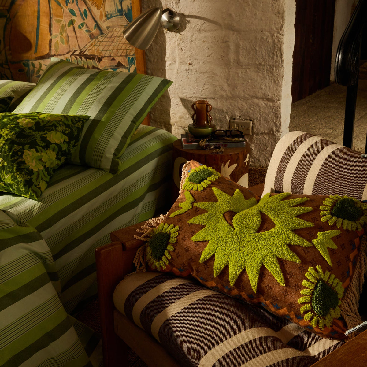 Brown lumbar cushion with chartreuse green tufted star motifs and fringe trim resting on a striped armchair