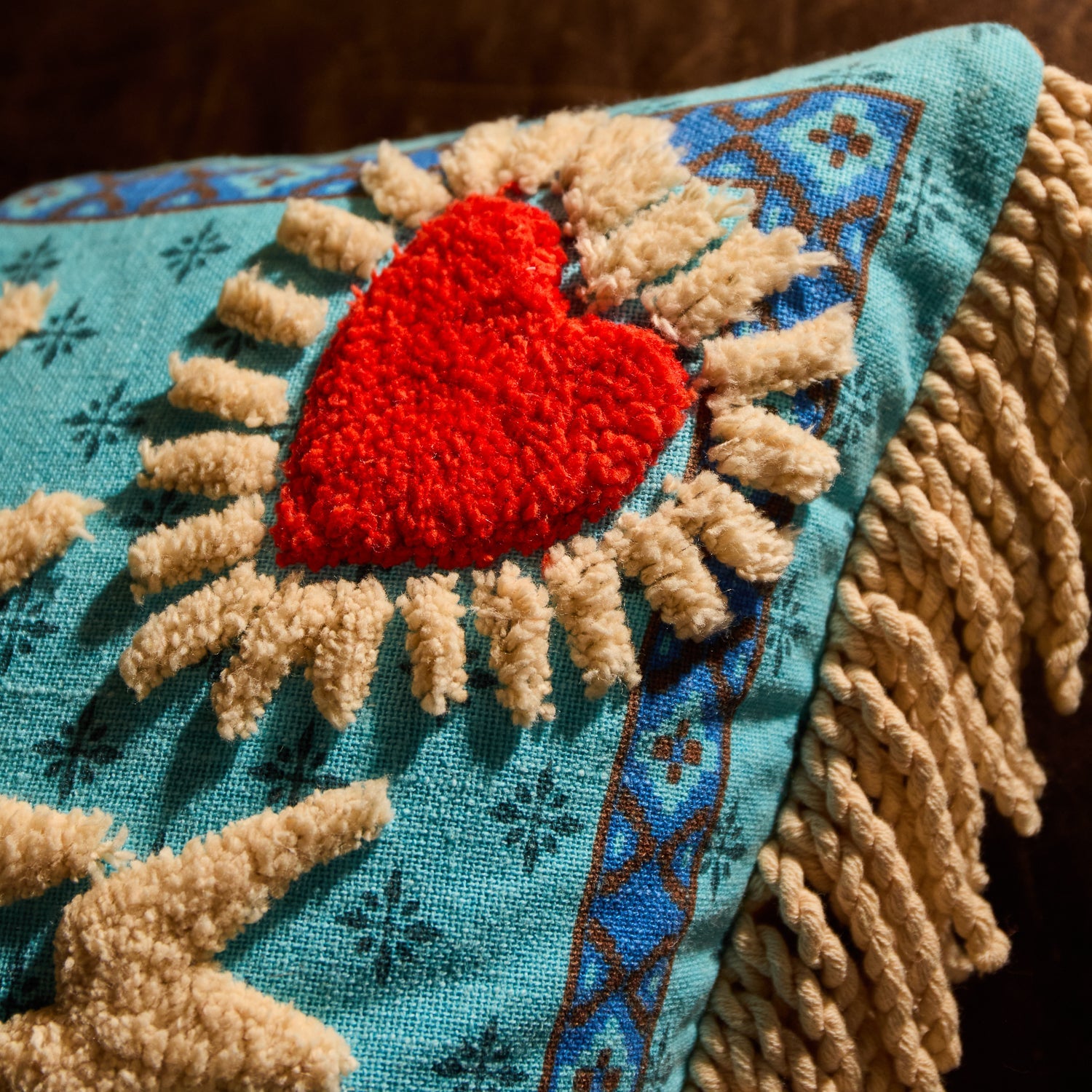 Close-up of red tufted heart motif and cream fringe trim on a turquoise blue reversible cushion
