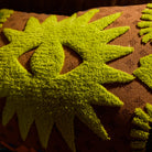 Close-up of lime green tufted star burst motifs on a brown printed cushion cover