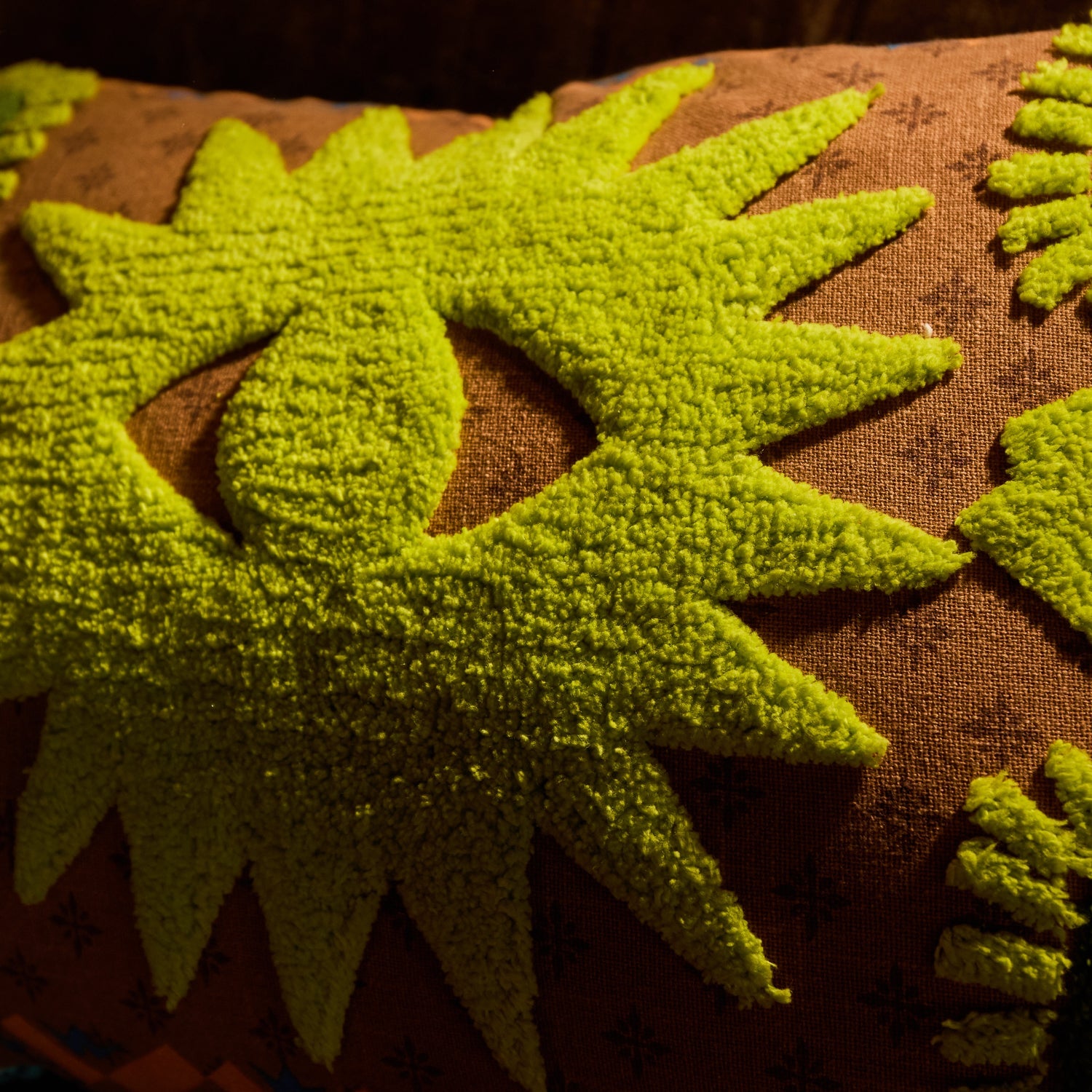 Close-up of lime green tufted star burst motifs on a brown printed cushion cover