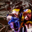 Close-up detail of silk scrunchie fabric texture showing iridescent multicolor shimmering surface finish