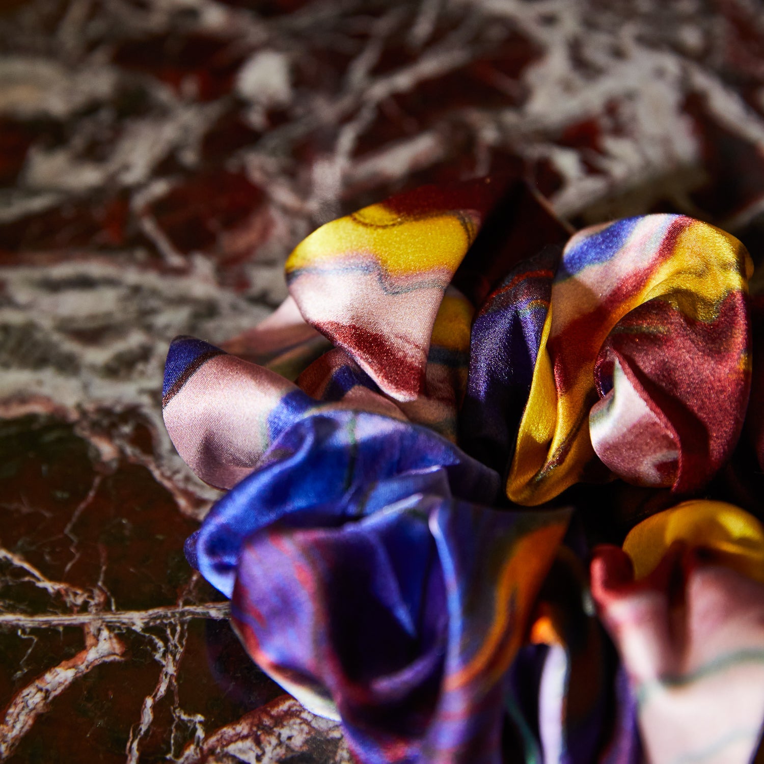 Close-up detail of silk scrunchie fabric texture showing iridescent multicolor shimmering surface finish