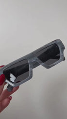 Gray glasses held by a hand with red nail polish against a plain background