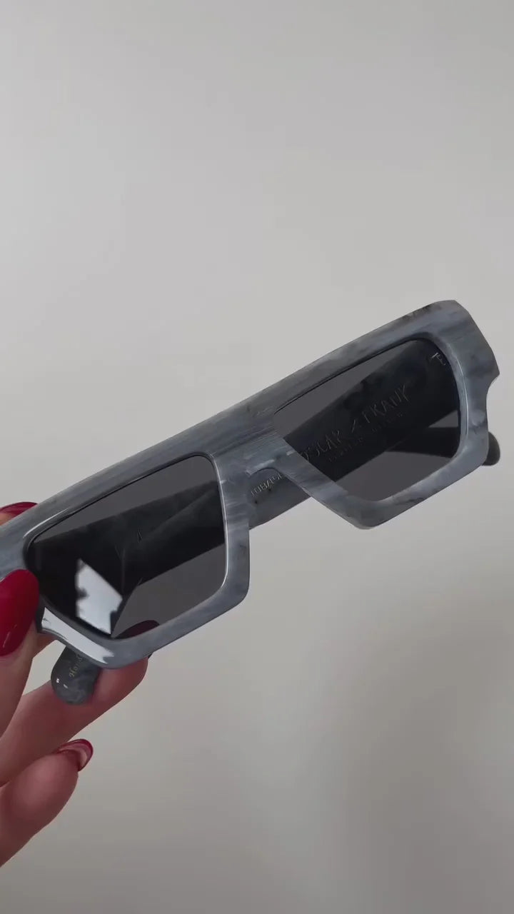 Gray glasses held by a hand with red nail polish against a plain background
