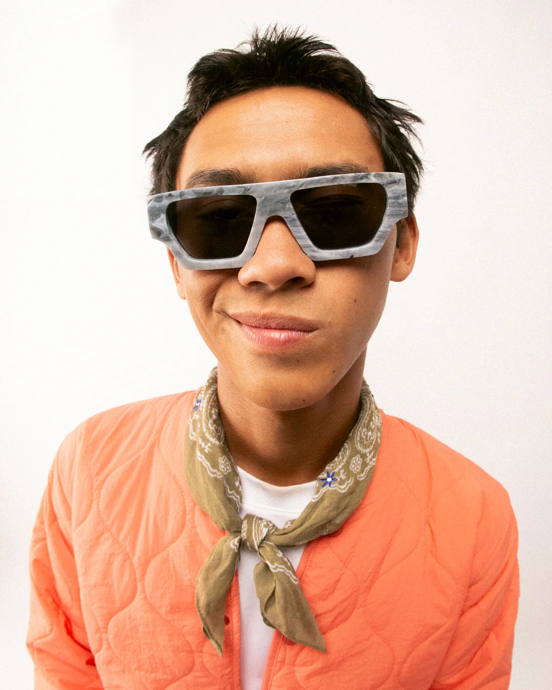 Person wearing sunglasses and an orange sweater with a bandana, on a white background
