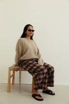 Seated view of Vali check pants displaying brown blue check pattern and wide leg cut